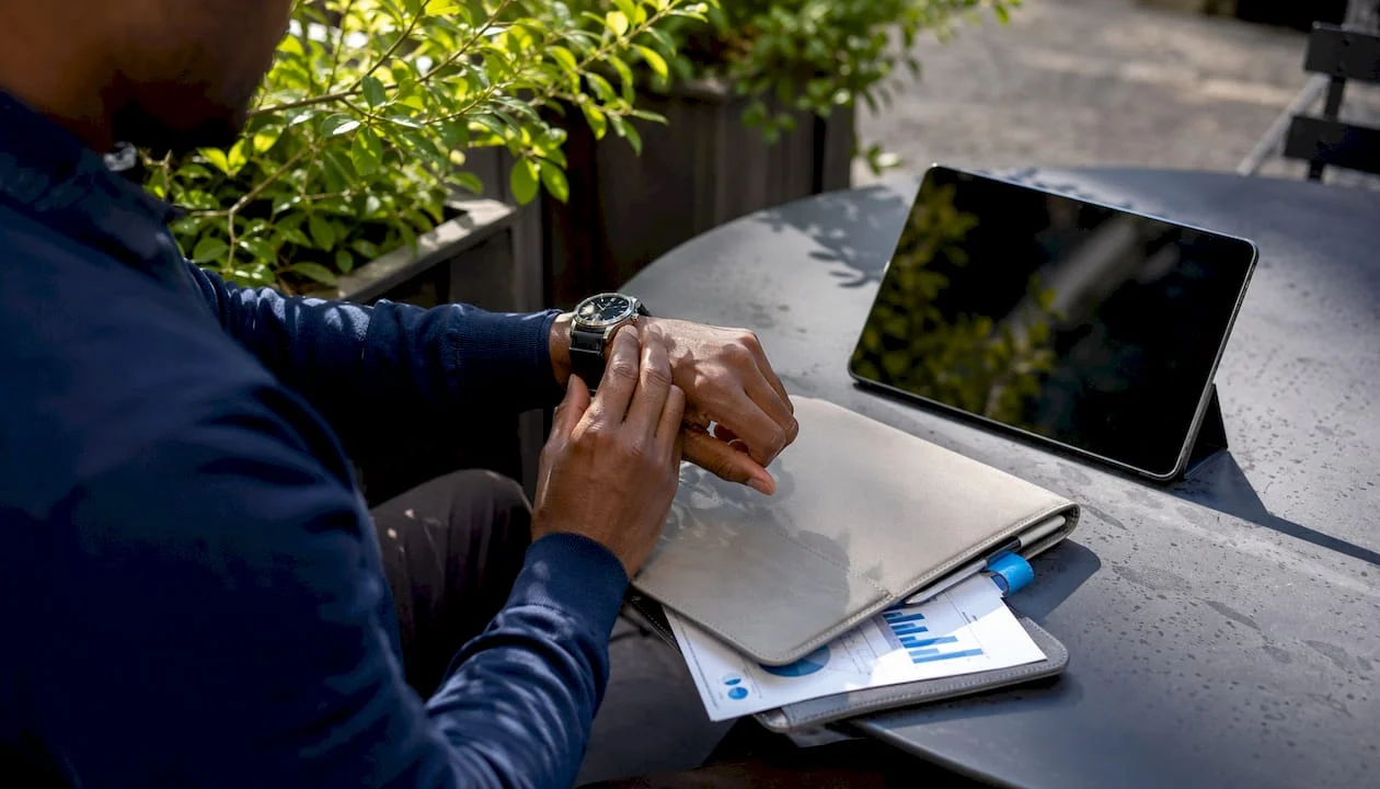 Hands adjusting watch beside tablet outdoors